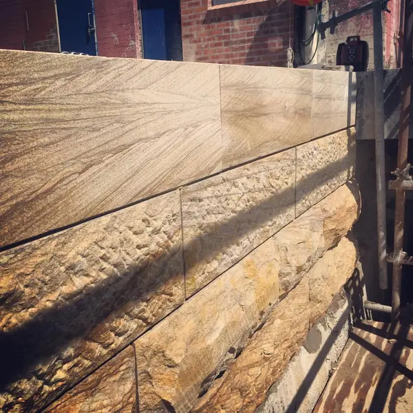Completed sandstone garden edge wall with hedge backdrop