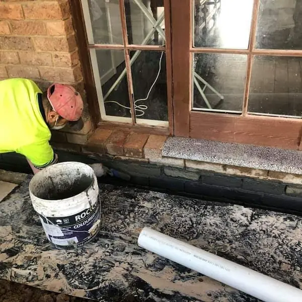 Worker applying waterproofing at base of heritage building