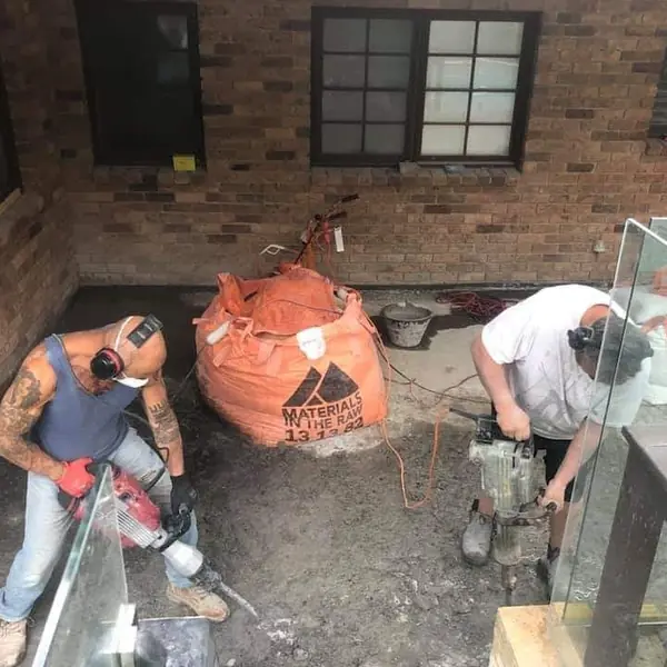 Two workers using jackhammers on concrete foundation