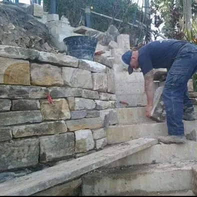Worker building stone retaining wall with steps