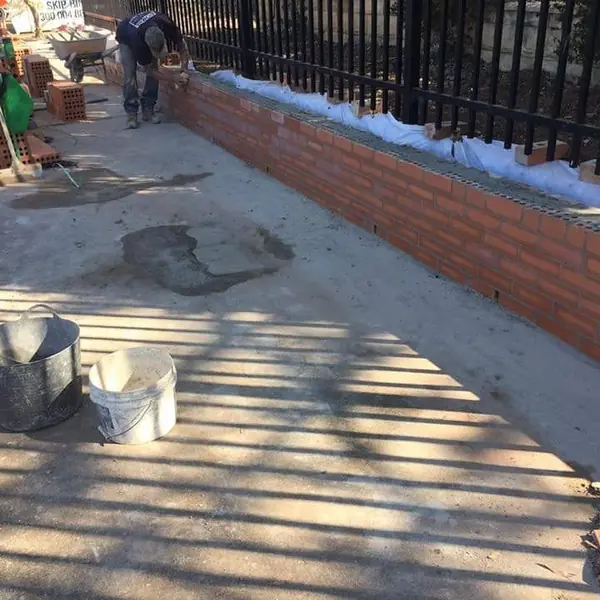 Worker building new brick boundary wall with waterproofing