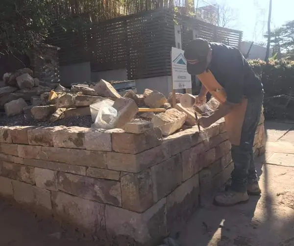 Stonemason building sandstone garden wall in sunlight