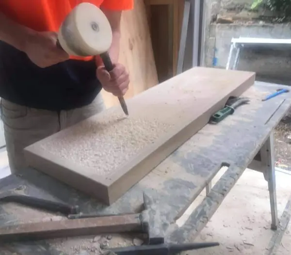 Craftsman hand-dressing sandstone slab with mallet and chisel