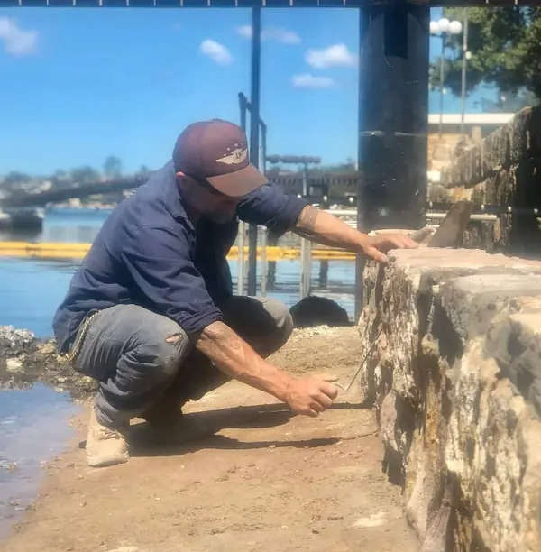 Stonemason repointing sandstone seawall at harbour wharf