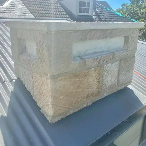 Sandstone chimney stack nearing completion on rooftop