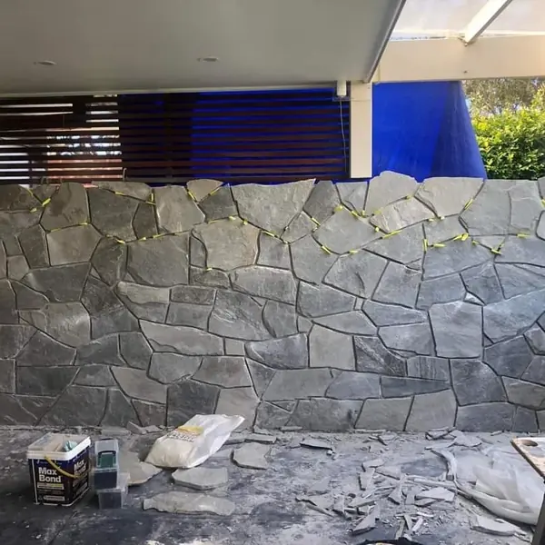 Stone crazy paving wall with garden hedge backdrop